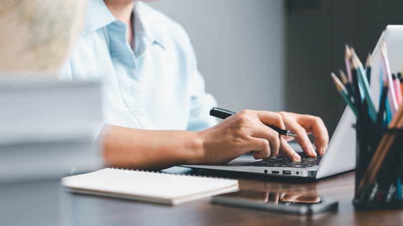 Close up of a person typing on a computer and taking notes